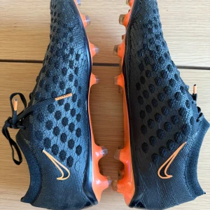 Svarta Nike fotbollsskor med orange detaljer - Säljer ett par svarta Nike phantom i storlek 44, dom är i bra skick och är använda ett fåtal gånger! Denna modell av phantom är inte så vanlig längre och modellen är svår att få tag i!