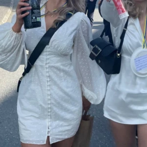 Adoore Florence dress - Superfin vit kort klänning med v-ringning, puffiga långärmar och små prickar i tyget. Klänningen har knappar framtill och markerad midja som ger en snygg siluett. Perfekt för sommarens alla tillfällen! Använd fåtal gånger och i superfint skick.