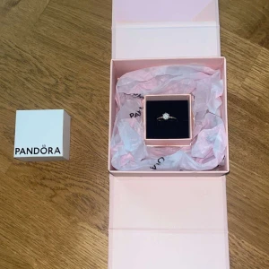 Pandora ring med stor sten - Snygg ring från Pandora i guldton med en stor, glittrande sten i mitten. Ringen har en klassisk och elegant design som verkligen sticker ut. Kommer i original ask och är perfekt som statement piece. Storlek 52 (16,5). Köpt för 1200 för endast några månader sen. Pris kan diskuteras.