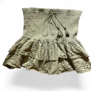 Beige volangkjol med snörning - Supersöt beige kortkjol med volanger och broderade detaljer. Kjolen har smock i midjan och en snygg snörning med tofsar framtill. Perfekt för dig som gillar en romantisk och bohemisk stil.