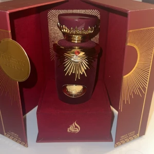 Lattafa Sakeena Eau de Parfum 100ml  - Exklusiv parfym i en mörkröd sammetsklädd flaska med guldiga detaljer och en röd sten. Flaskan har en unik form med kunglig krona och solstråle-motiv. Kommer i en matchande lyxig ask med gulddetaljer och orientaliska inslag. Endast testad