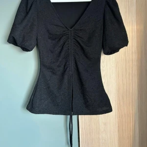 Svart blus med puffärm  - Super fin svart blus med puffiga korta ärmar och v-ringning. Blusen har en liten slits framtill och en väldigt figurnära passform. Köpt på bikbok. Säljer pga att den inte passar längre, har använt fåtal gånger så är i mycket bra skick