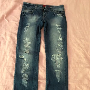 Blå slitna jeans från Vero Moda - Säljer ett par blå jeans från Vero Moda med låg midja och snygga slitningar båda fram och baktill. Otroligt snygga men tyvärr för korta på mig. Mått finns på bilderna
