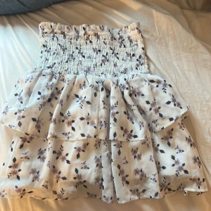 Vit blommig volangkjol - Supersöt kort kjol i vitt med lila blommor, de är en kjol men kan även användas som topp, knappt använd, skriv om fler bilder💕