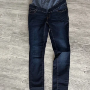 Mörkblå gravidjeans från Noppies W27 - Snygga mörkblå gravidjeans från Noppies storle W27 med hög midja och mjuk stretchig mudd över magen. Klassisk femficksmodell med kontrastsömmar och raka ben. Perfekta för dig som vill ha både stil och komfort under graviditeten.