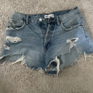 Blå slitna jeansshorts från Zara - Korta Shorts från Zara. Skulle nog haft dessa vid stranden under bikinin tex inte ute  i stan, då de är korta vid rumpan. Är Xs men passar mig som ändå brukar mellan S/Xs