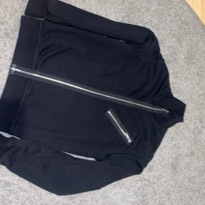 Svart jacka från Dsquared2 med tryck - Svart jacka från Dsquared2 med stort vitt tryck på ryggen och cool diagonal dragkedja framtill. Jackan har en extra dragkedjeficka på bröstet och hög krage. Tillverkad i mjukt bomullsmaterial, perfekt för en streetwear-look.