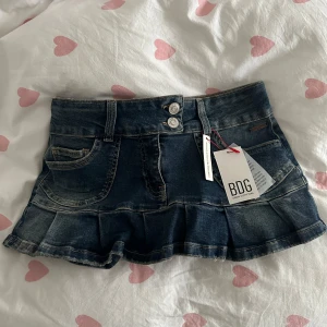 mini jeanskjol från BDG - Supersöt mörkblå jeanskjol från BDG med volangkant och dubbla knappar framtill. Kjolen har klassiska fickor både fram och bak, med snygga broderade detaljer på bakfickorna. Helt ny, prislappen är kvar!🩷