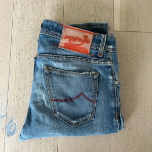 Blå jeans från Jacob Cohen - Säljer ett par Jacob Cohen jeans i modell 622c, storlek 32. De är otroligt sköna, riktigt mjuka och sitter fortfarande bra trots att de är mycket använda. Det här är premiumjeans med riktigt snygg tvätt och passform. Även om de är slitna har de mycket liv kvar . Skador/slitage: Slitna och små hål på rumpan Slitage på bakfickorna Hål på ena knät Litet hål och lagningar i skrevet (syns ej när man har dem på) Patchen bak är sliten.  Lite slitet längst ner. Nypris är runt 5500-7000 kr 