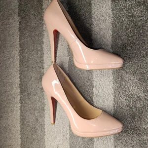 Rosa klackar från Christian Louboutin - Snygga rosa klackar från Christian Louboutin med klassisk röd sula. Skorna har spetsig tå, hög klack och är tillverkade i glansigt skinn. Perfekta för dig som vill sticka ut med en elegant och tidlös look.
