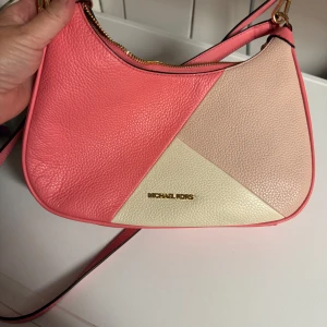Michael Kors rosa axelväska i skinn - Snygg axelväska från Michael Kors i färgblockad design med rosa, ljusrosa och beige partier. Väskan är gjord i präglat skinn och har guldfärgad logga framtill samt dragkedja upptill. Perfekt storlek för det viktigaste och en riktigt trendig accessoar.