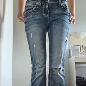 Miss me jeans - Säljer ett par blå bootcut jeans med snygga slitningar och detaljerade bakfickor med kontrastsömmar. Jeansen har låg midja och klassisk femficksdesign. Perfekta för dig som gillar en avslappnad men trendig look. Använda runt tre ggr och säljs för att dem är lite korta, är 170cm!!