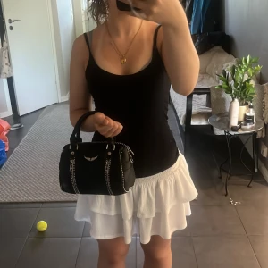 Zadig & Voltaire svart handväska i skinn - Säljer en svart handväska från Zadig & Voltaire i grained skinn med coola silverdetaljer och dragkedjor. Väskan har ett emblem framtill, bred axelrem med text och små nitar längs kanterna. Perfekt storlek för det viktigaste och riktigt snygg att bära både i handen och över axeln.