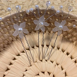 Hårnålar med vita blommor och pärlor - Tre hårnålar med vita blommor i plast, dekorerade med pärlor och glittriga stenar på silverfärgade ståltrådar. Perfekt för att ge en romantisk och söt touch till frisyren. Blommorna har fem kronblad och en pärla i mitten.