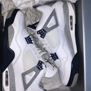 Nike Air Jordan 4 White Oreo - Säljer ett par Nike Air Jordan 4 i färgen White Oreo. Skorna har vit ovandel i skinn med grå och svarta detaljer, meshpaneler och speckled gråa inslag på sidor och sula. Klassisk Jumpman-logga på plösen och häl. Perfekta för dig som vill sticka ut med en ikonisk sneaker.