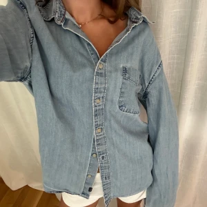 Ljusblå jeansskjorta från East West - Ljusblå jeansskjorta från East West. Skjortan har klassisk krage, knappstängning framtill och en bröstficka. Tillverkad i mjukt jeanstyg med diskreta kontrastsömmar. 