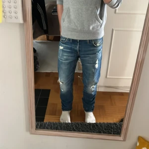 G-Star Raw 3301 blå jeans med slitningar - Säljer ett par G-Star Raw 3301 jeans i blå tvätt med snygga slitningar och distressed detaljer. Klassisk femficksmodell med raka ben och normal passform. Jeansen har coola slitna partier och tydliga kontrastsömmar. Ordinarie pris: 1599 kr  mitt pris: 499 kr. Perfekta för en avslappnad streetstil.