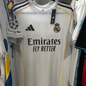 Real Madrid Trent 12 Champions League fotbollströja - Snygg vit Real Madrid fotbollströja från Adidas med svarta detaljer och gula inslag. Champions League-märke på ärmen, tryck med 'Trent 12' på ryggen och klubbmärke på bröstet. Tillverkad i lätt och ventilerande material, perfekt för match eller träning. (Har varit utloggad i över ett halvår, och har glömt bort lösenordet, därför den dåliga reviewen, men nu lovar jag att skicka iväg den tidigt) :)