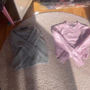 Grå fluffig och rosa stickad tröja - Två mysiga tröjor: en grå fluffig stickad tröja med rund hals och en ljusrosa stickad tröja med ribbade muddar och rund hals. Perfekta för kyliga dagar och supermjuka mot huden. Båda har lång ärm och klassisk passform.