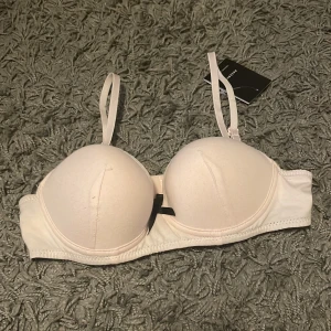 Ljus-rosa BH med svarta detaljer - Snygg ljusrosa BH som kan också uppfattas som vit från Reserved med vadderade kupor och justerbara axelband. Toppen har en svart rosett framtill och svarta detaljer längs kanterna för en cool kontrast. Perfekt att bära under en skjorta eller som den är till jeans. För 10-11 år 146/152cm med size range 134-164. 