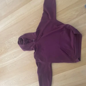 Vinröd hoodie från BikBok - Mysig vinröd hoodie från BikBok med huva och snörning. Tröjan har en stor magficka och är tillverkad i mjuk bomullsblandning. Perfekt för chill dagar eller när du vill ha en avslappnad stil.