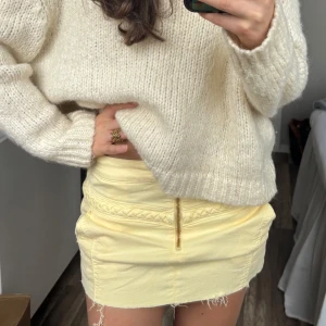 Gul kort jeanskjol med dragkedja - Supersöt ljusgul kort jeanskjol med råa kanter och en synlig guldfärgad dragkedja framtill. Kjolen har en flätad detalj längs höften som ger en extra touch🥰