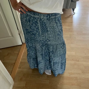 Blå långkjol med mönster - blå långkjol med mönster. Kjolen har resår i midjan och är luftig och snygg till sommaren. Storlek L men passar mig bra som bär S/M. Köpt på en marknad.