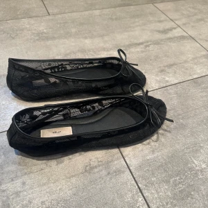 Svarta spetsballerinor från Nelly - Snygga svarta ballerinaskor från Nelly i spets med rosett framtill. Skorna har rund tå och transparenta partier som ger en trendig look. Perfekta för dig som gillar en feminin och stilren stil. Säljer pågrund av att dom är stora i storlek, skulle säga att dom passar någon med storlek 37