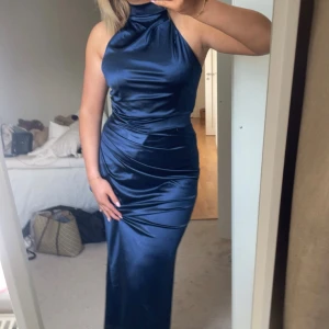 Marinblå långklänning i satin - Snygg marinblå långklänning i glansigt satinmaterial med hög hals och ärmlös design. Perfekt för dig som vill sticka ut på balen! Halterneck så går att knyta i halsen med öppen rygg (går att ha BH under)💞 Köpte av en tjej på plick (sista bild lånad) och står inte märke men köpte för 1250, använd endast en gång! Strl M/38