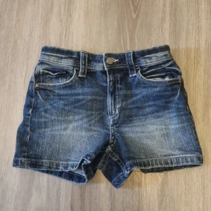 Blå jeansshorts från H&M - Snygga blå jeansshorts från H&M i klassisk femficksmodell. Shortsen har normal passform, bälteshällor och knäppning fram. Bakfickorna har lock med knappdetalj. Perfekta för sommaren och lätta att matcha med allt. 