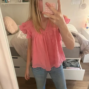 Rosa blus med volangärmar - Supersöt rosa blus med volangärmar och v-ringning. Lätt och luftig modell med fina spetsdetaljer upptill. Perfekt för vår och sommar, passar till både jeans och kjol. Blusen har en lös passform och är tillverkad i ett tunt bomullstyg.