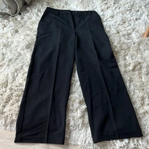 Svarta vida kostymbyxor - Snygga svarta kostymbyxor med vida ben och pressveck. Klassisk look med hällor för bälte och diskreta sidfickor. Perfekta för en clean och stilren outfit. Från Bik Bok i strl M och är som nya!