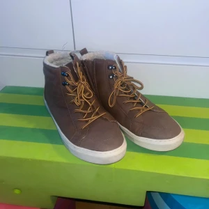 Bruna vinterkängor från Zack, stl 39 - Bruna kängor från Zack med vit fuskpälsfoder, snörning och dragkedja på sidan. Snygg kontrast mellan de gula skosnörena och den bruna ytan. Perfekta för kalla dagar med sin varma insida och robusta vita sula.