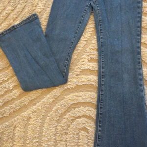 Blå bootcut jeans - Säljer ett par klassiska blå jeans med bootcut-modell. Jeansen har en snygg tvätt och raka ben som blir vidare nedtill. Perfekta för dig som gillar en retrostil och vill ha ett par bekväma jeans med lite extra sväng i benen.