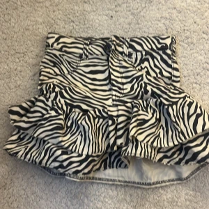 Zebramönstrad volangkjol från Dr Denim - Supersnygg kort kjol från Dr Denim med svartvitt zebramönster och volangkant. Kjolen har klassisk jeanslook med fickor fram och bak samt knapp och dragkedja. Perfekt statement piece för dig som vill sticka ut. Sytt om den själv därav priset, ursprungligen jeans och därav storlek L . Men nu bör den ör kjol sitter den som en S.