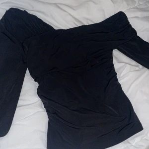 Svart offshoulder top Gina Tricot - Helt ny snygg svart offshoulder topp från Gina Tricot i stretchigt material som har använts 1 endast gång. Toppen har långa ärmar och perfekt för dig som gillar en stilren och trendig look.