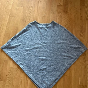 Grå poncho-tröja från Cellbes - Mysig grå poncho-tröja från Cellbes i mjukt stickat material. Tröjan har en lös passform och snygga knappar på ena axeln som detalj.