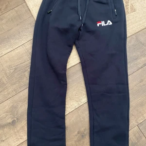 Svarta mjukisbyxor från FILA, stl S - Svarta mjukisbyxor från FILA med broderad logga på vänster lår. Byxorna har dragsko i midjan, fickor med dragkedja och är gjorda i mjukt bomullsmaterial. Perfekta för chill eller träning, sitter skönt och har en normal passform. Priset går att diskutera 
