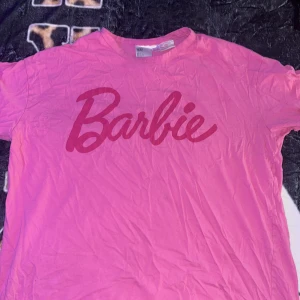 Rosa Barbie t-shirt från H&M - Säljer en rosa t-shirt från H&M med stort Barbie-tryck framtill. Klassisk passform med rund hals och korta ärmar. Perfekt för dig som älskar Barbie och vill sticka ut med en färgglad look.