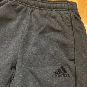 Grå mjukisbyxor från Adidas XS - Mörkgrå mjukisbyxor från Adidas i storlek XS. Byxorna har resår i midjan och Adidas-logga broderad på ena benet. Tillverkade i mjukt material som är perfekt för chill eller träning. Klassisk och enkel design med fickor på sidorna.