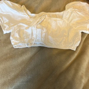 Vit croppad blus från Zara - Superfin vit croppad blus från Zara med puffiga korta ärmar och elastiska detaljer vid midja och ärmslut. Snygg fyrkantig ringning och lätt glansigt tyg som ger en fräsch look. Perfekt att styla med höga jeans eller kjol.