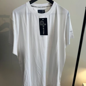 Vit t-shirt från Pelle P med tryck - Vit t-shirt från Pelle P i mjuk bomull med stort svart logotryck och koordinater på ryggen. Klassisk passform med rund hals och korta ärmar. Diskret logga även på ärmen. Perfekt för en clean och stilren look.