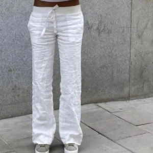 Vita linnebyxor ALOBHA  - Säljer ett par fräscha vita linnebyxor med låg midja och snörning i midjan. Byxorna har raka ben och är tillverkade i ett linnematerial, perfekta för varma dagar. De har en avslappnad passform och ger en chill vibe till din outfit.