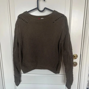 Brun stickad tröja från H&M - Säljer en brun stickad tröja från H&M i storlek M. Tröjan är grovstickad i 100% bomull med snygga håldetaljer vid axlar och sidor. Den har rund halsringning och långa ärmar, perfekt för lager-på-lager under höst och vinter.