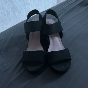 Svarta klackar strl 40 - Snygga svarta sandaler med kilklack och breda remmar. Skorna har öppen tå och plattformsula, vilket ger både höjd och komfort. Perfekta för dig som vill ha en stilren och enkel look med lite extra edge.