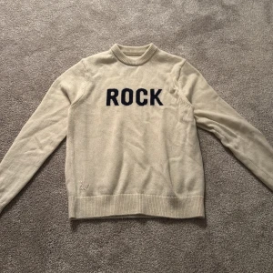 Beige tröja med texten ROCK - Säljer en beige tröja med texten ROCK i svart på framsidan. Tröjan har en rund halsringning och långa ärmar. Perfekt för en avslappnad stil.