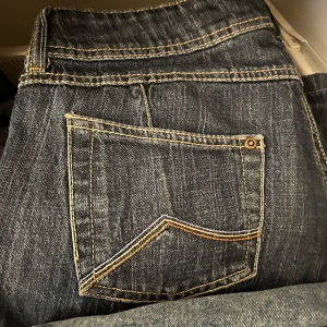 Mörkblå jeansbyxor - Säljer ett par mörkblå jeansbyxor som är oanvända med klassisk femficksdesign och kontrastsömmar. Byxorna har en rak passform och är tillverkade i slitstarkt denim. Funkar som lowwaist och den är bootcut!Skulle säga att storleken är 38.