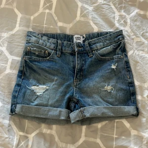 Jeansshorts från lager 157 - Snygga jeansshorts från lager 157 i blå denim med slitna detaljer och uppvikta ben. Perfekta för en avslappnad stil. De har klassisk femficksdesign och knappgylf.