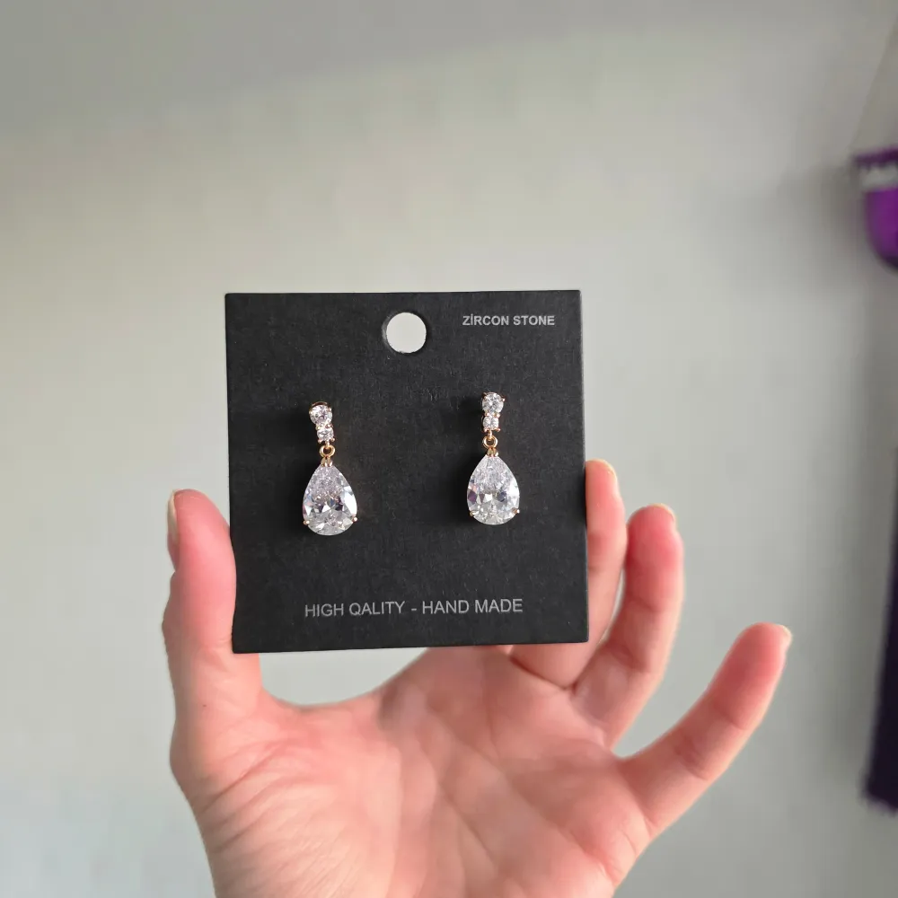 Snygga handgjorda örhängen med stora droppformade zirkonstenar. De har en elegant design med flera mindre stenar ovanför den stora, vilket ger en lyxig känsla. Perfekta för att ge en extra touch av glamour.. Asusteet.