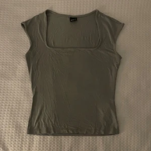 Gina tricot topp - Snygg grå topp från gina med fyrkantig urringning och korta ärmar. Perfekt för en stilren look. Passar bra till både jeans och kjol.